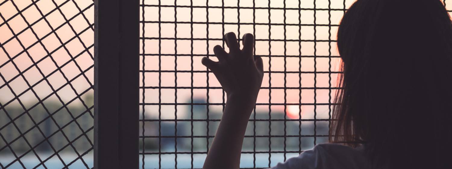 Young woman with a hand on fencing looking outside from inside