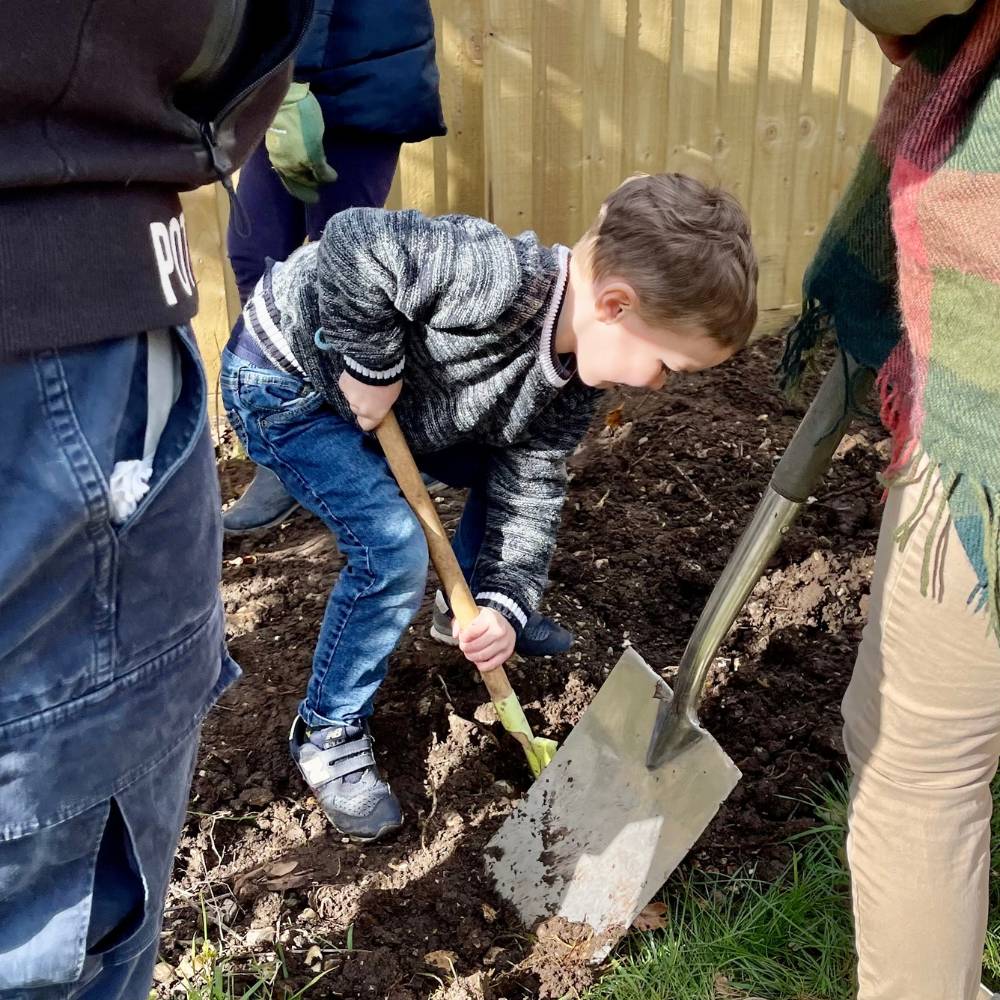 Young boy digging soil with a spade outside in St Mary's Churchyard