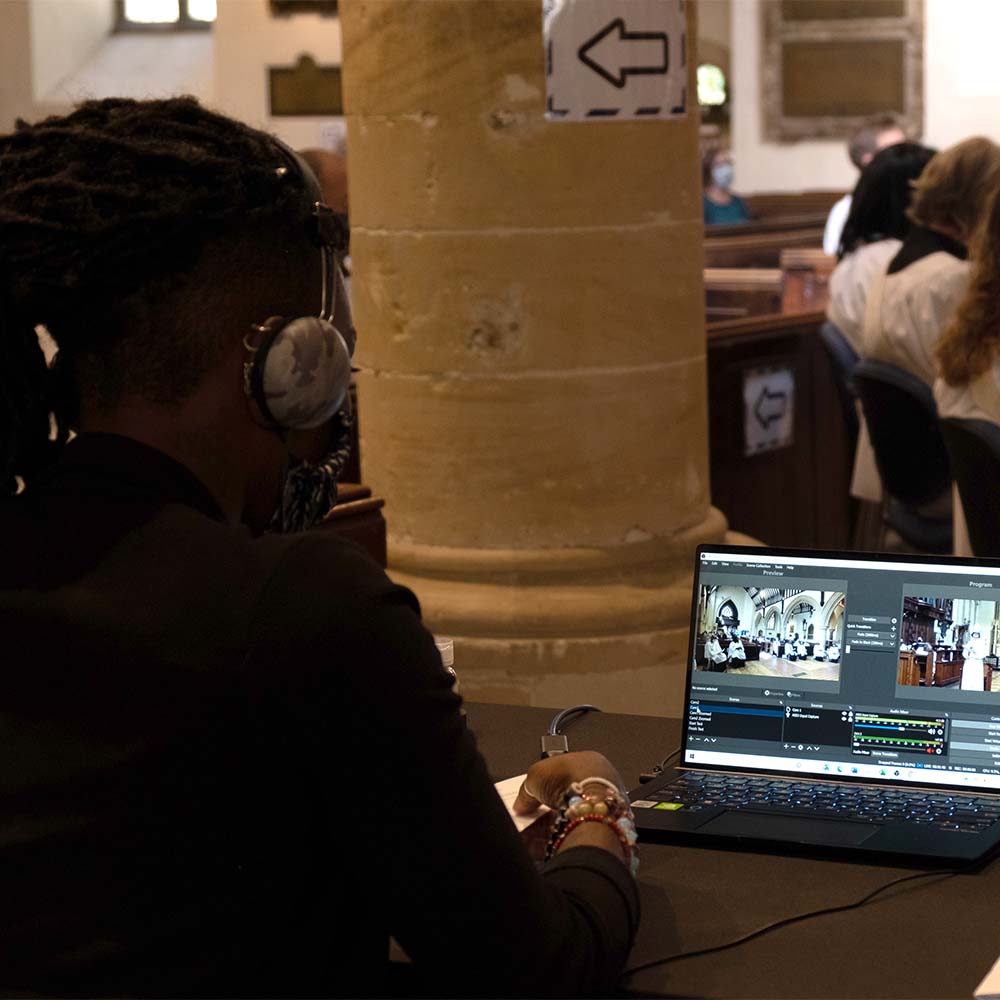 A woman sits by her laptop in a church service, running a livestream feed