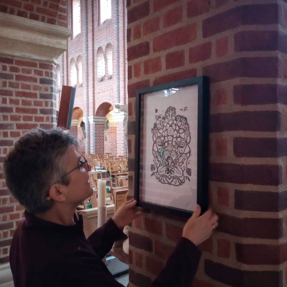 Print art in black frame being hung on a brick wall in St John's Church Newbury