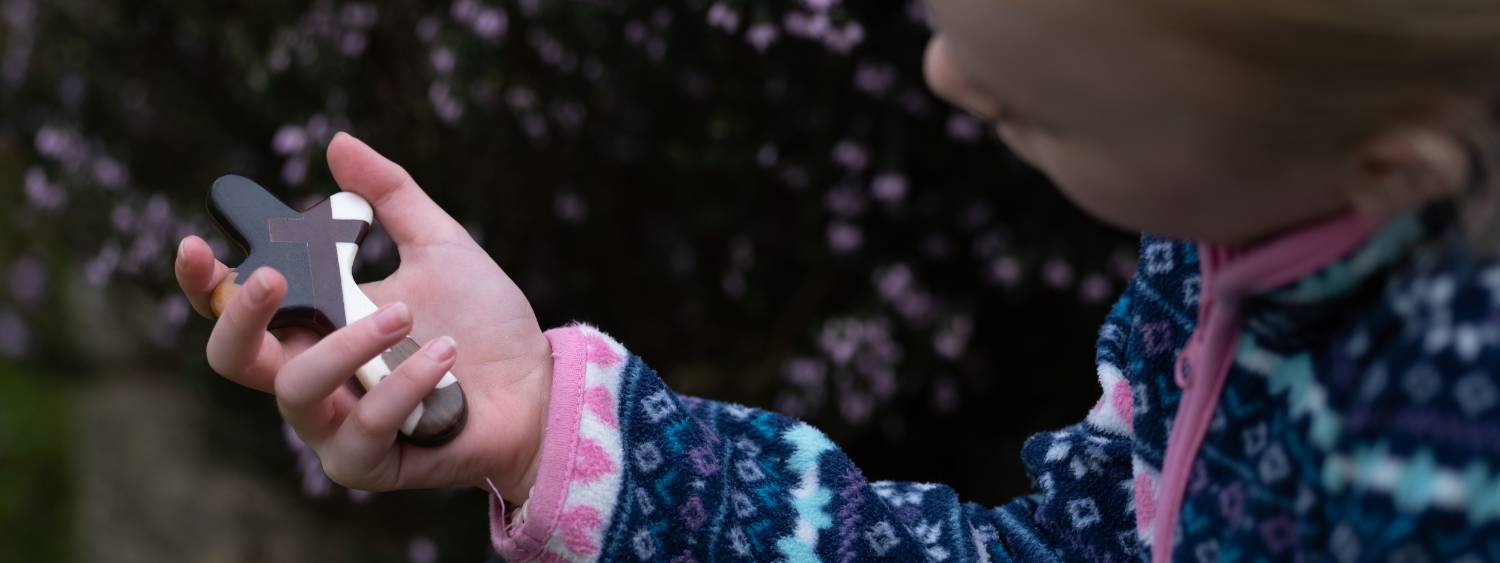 Young girl holds a wooden prayer cross in her hand and is looking at it.