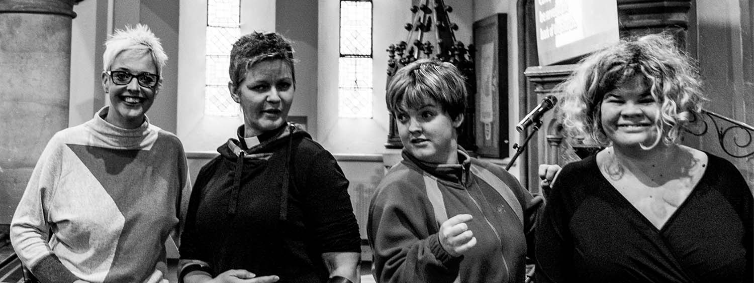 Four women are standing in a row in a church smiling, one woman is wearing a clerical collar, two are young adults..