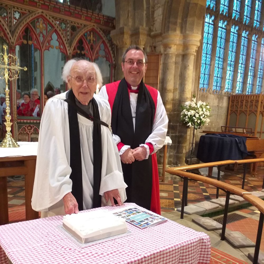 Michael Campling stands with the Bishop of Dorchester behind a table with a large cake.