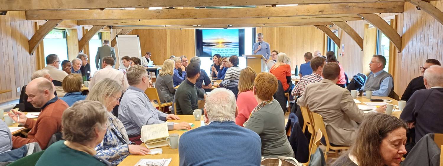 Chaplains sit at tables at Christ Church research centre listening to a speaker.