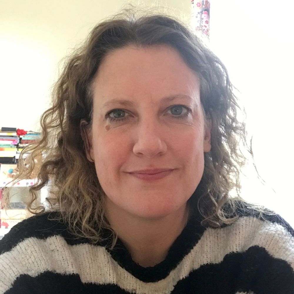 headshot of Amy, she has bobbed curly hair and is wearing a black and white striped top.