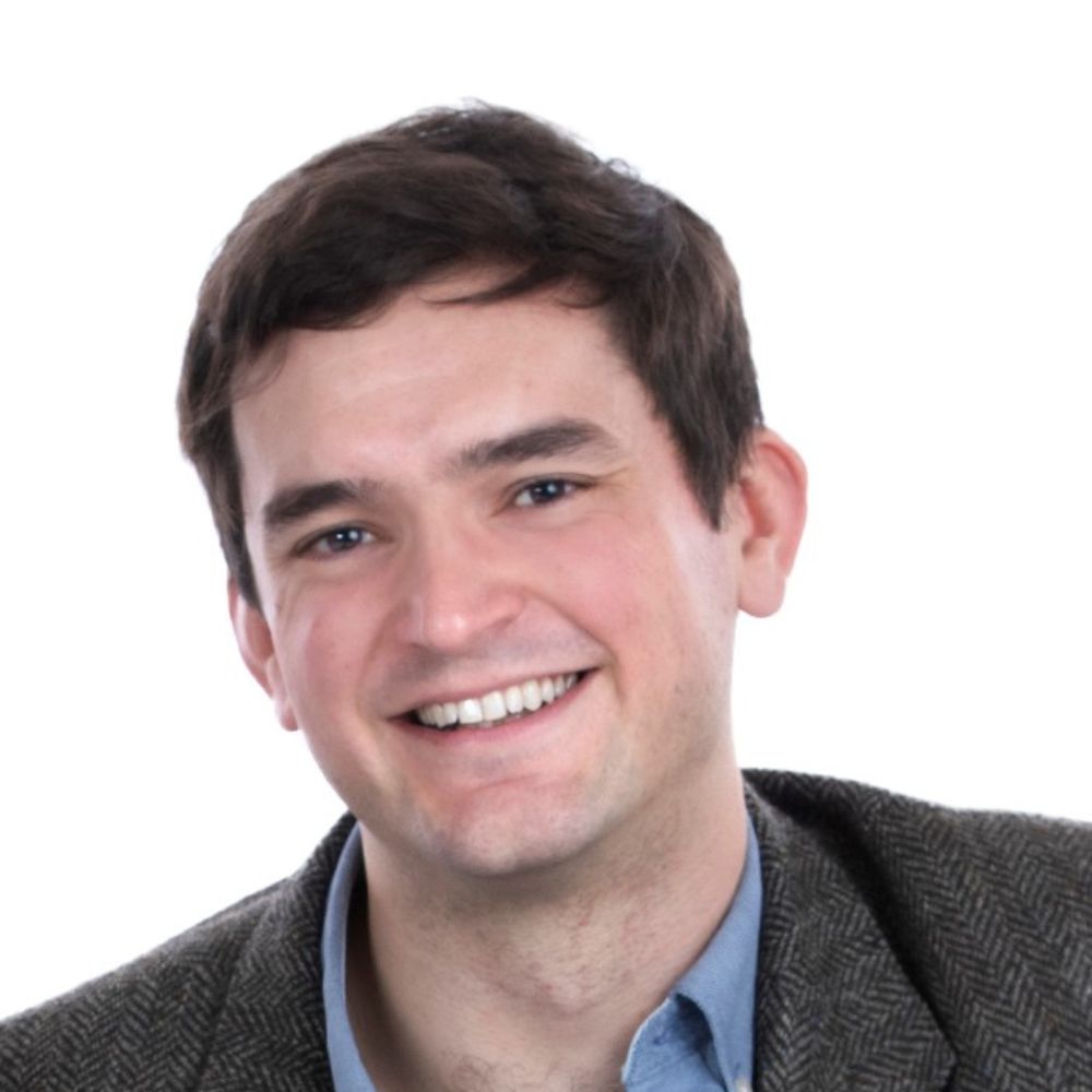 headshot of Sam, he is smiling and wearing a blue shirt and dark jacket