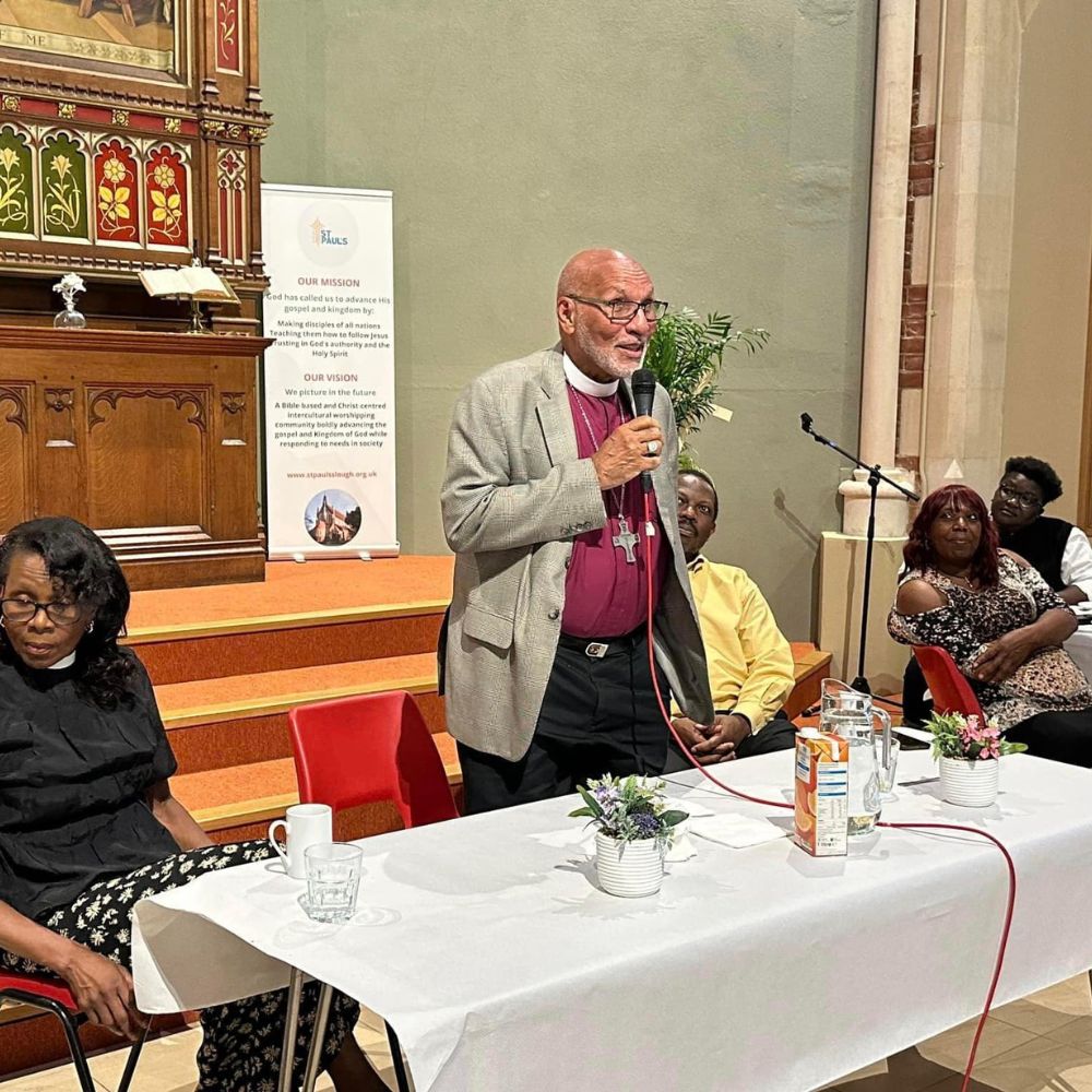 Archbishop Howard Gregory stands speaking into a handheld microphone to a group of clergy and lay people at St Paul's Church, Slough. 